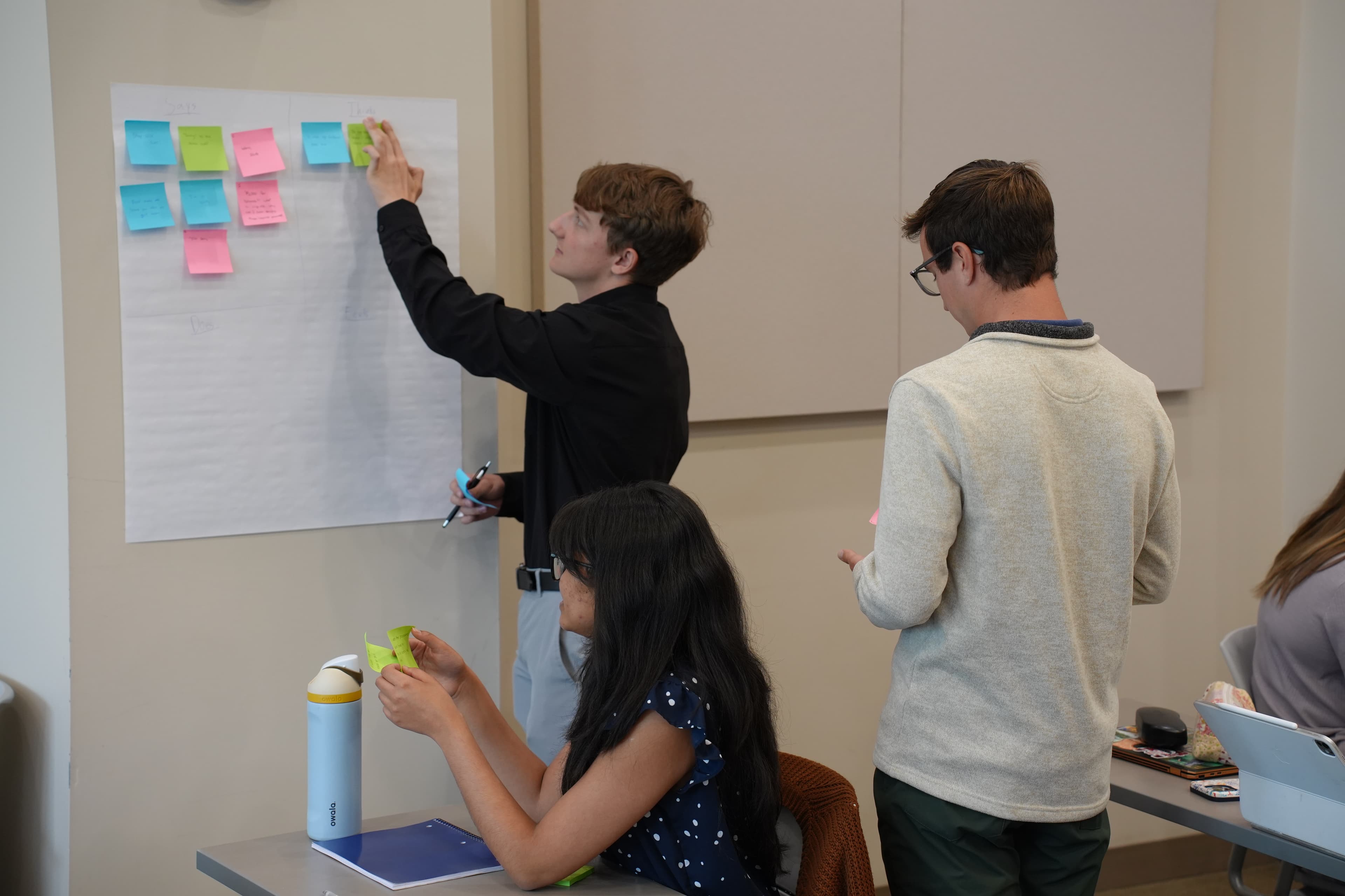 Students brainstorm using sticky notes on a wall